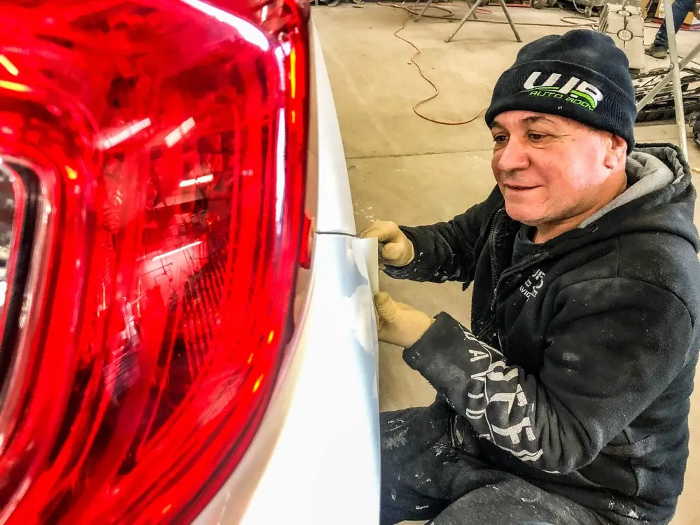 WR Auto Body technician smoothing a repaired rear panel next to a car's tail light